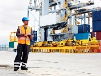 Un employé d'un port tient une tablette entre ses mains près d'un bateau de cargaison