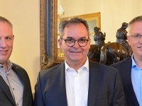 Trois personnes en tenue professionnelle posant à l’intérieur, devant un miroir et une sculpture décorative.