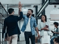 Groupe de collègues dans un bureau industriel, dont deux se donnent un high‑five tandis qu’une autre personne tient des documents et qu’une quatrième est assise à l’arrière avec un ordinateur portable.