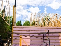 Structure de bâtiment en construction avec des panneaux isolants OSBLOCK et une charpente en bois, accompagnée d’un camion et de machinerie sur un chantier entouré d’arbres.