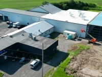 Vue aérienne d’une usine avec plusieurs bâtiments, stationnements et véhicules, montrant un agrandissement en cours avec une zone de construction et un chariot élévateur orange.