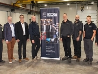 Groupe de personnes debout dans un vaste atelier industriel, de part et d’autre d’une bannière EDS présentant des images d’équipement et de solutions d’étanchéité.