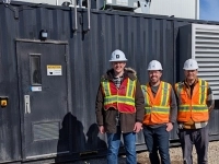 Trois personnes portant des casques de sécurité et des vestes haute visibilité debout devant une unité industrielle noire portant l’inscription « SKYRENU 50 » sur un site extérieur.