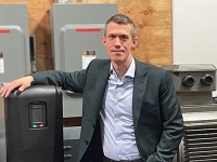 Personne debout dans un atelier industriel, posant à côté d’un équipement électrique et de machinerie. 