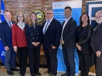 Groupe de sept personnes posant à l’intérieur devant des drapeaux, des bannières gouvernementales.