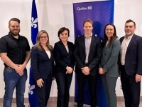 Groupe de personnes debout devant une bannière du gouvernement du Québec et un drapeau fleurdelisé dans une salle intérieure.