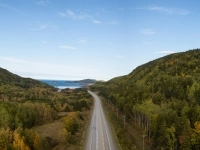 Route traversant une vallée entourée de collines boisées, avec la mer visible à l’horizon. 