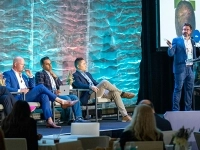 Présentation lors d’une conférence, avec une personne debout à un podium devant un écran affichant des images de cuir chevelu, et plusieurs personnes assises sur scène.