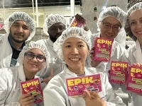 Groupe de personnes en tenue de production alimentaire tenant des emballages de produits EPIK dans une usine, devant un équipement de transformation.