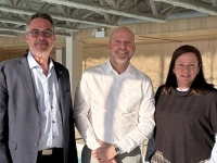 Trois personnes se tiennent dans une zone rénovée de l’hôtel entourée de matériaux en bois et d’un aménagement moderne. 