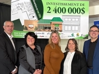 Cinq personnes posent devant un panneau annonçant un investissement de 2 400 000 $ pour un projet immobilier, accompagné d’un dessin architectural et de logos de partenaires. 