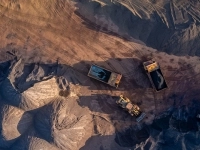 Vue aérienne d’un site minier où plusieurs camions et machineries lourdes déplacent et chargent des matériaux sur un terrain de sable et de gravier. 