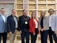 Groupe de personnes posant devant une structure murale en construction, accompagnées des drapeaux du Québec et du Canada, lors d’un événement officiel à l’usine Prestige Panel.